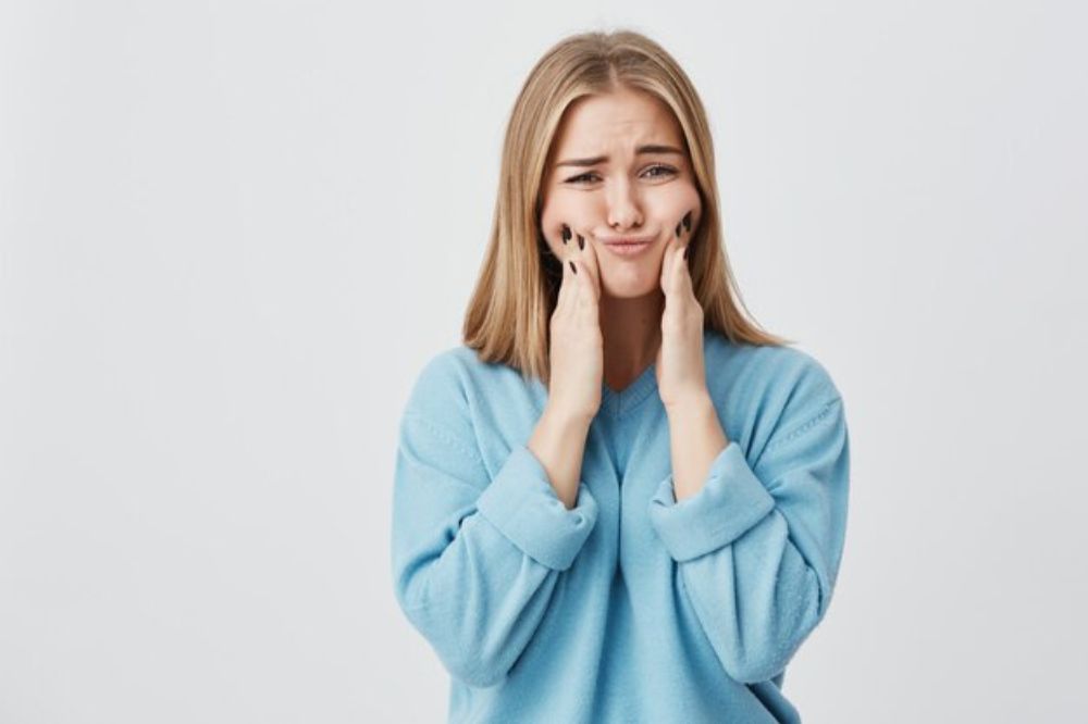 a girl is holding her teeth because of dental pain